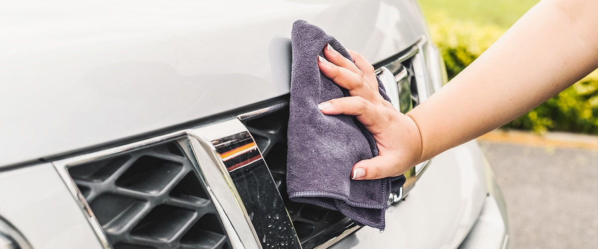 Hand wiping the front grille of a car with a microfiber cloth, showcasing car cleaning.