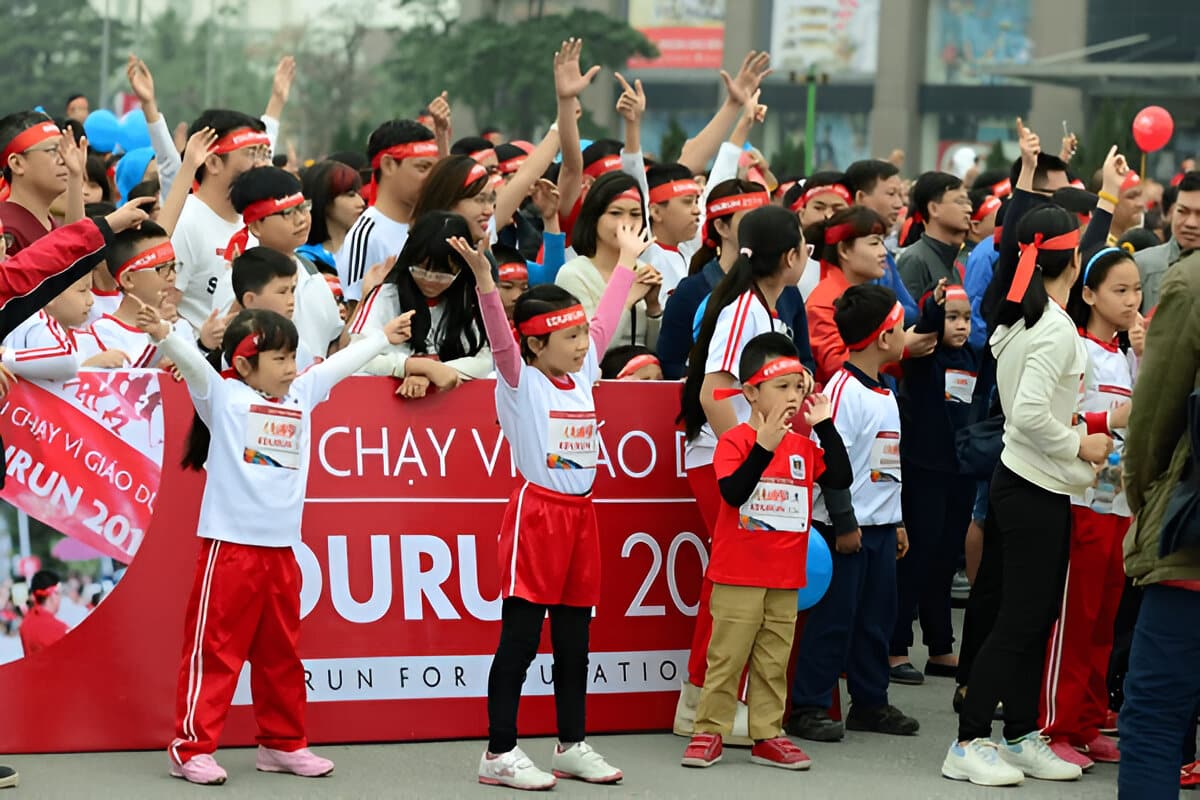 Large group of children and adults wearing red headbands participating in a fundraising fun run event.