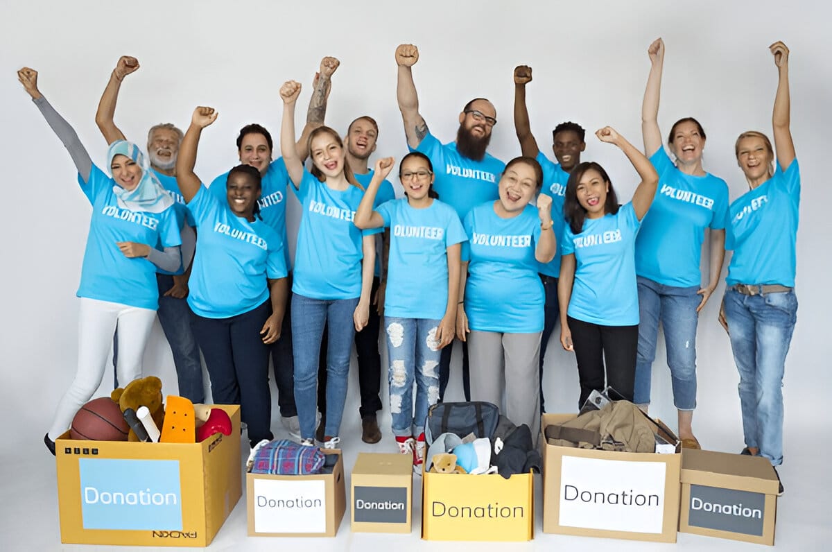 Group of enthusiastic volunteers in blue t-shirts celebrating with donation boxes filled with items.How to Start a Fundraiser: Set Goals, Budgets & Strategies