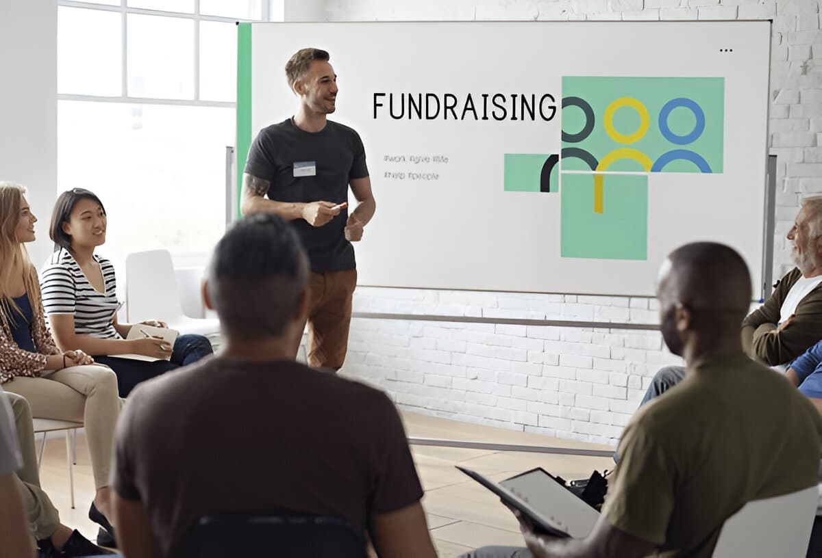 Group meeting discussing fundraising strategies, with a presenter standing near a whiteboard that says 'Fundraising.