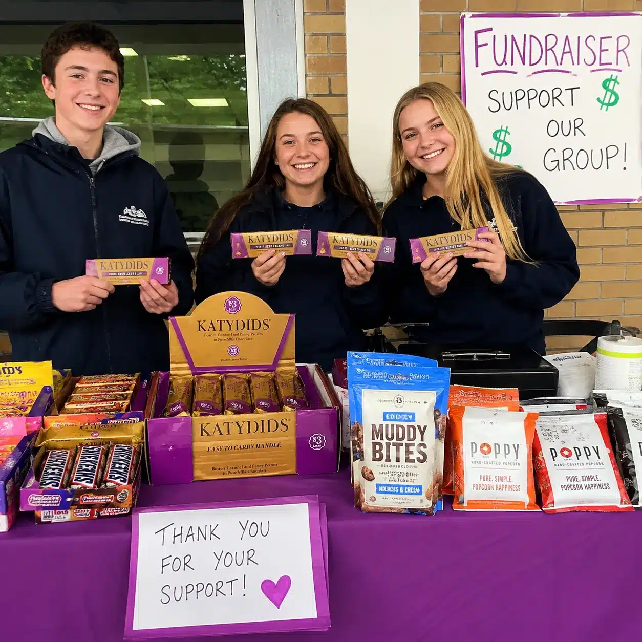 Students selling Katydids chocolate bars and snack products at a fundraising table during a community fundraiser event.